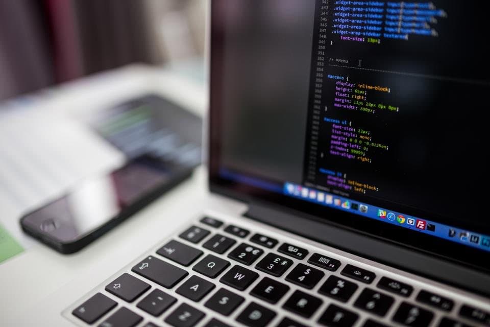 Laptop showing source code, with a phone on the desk